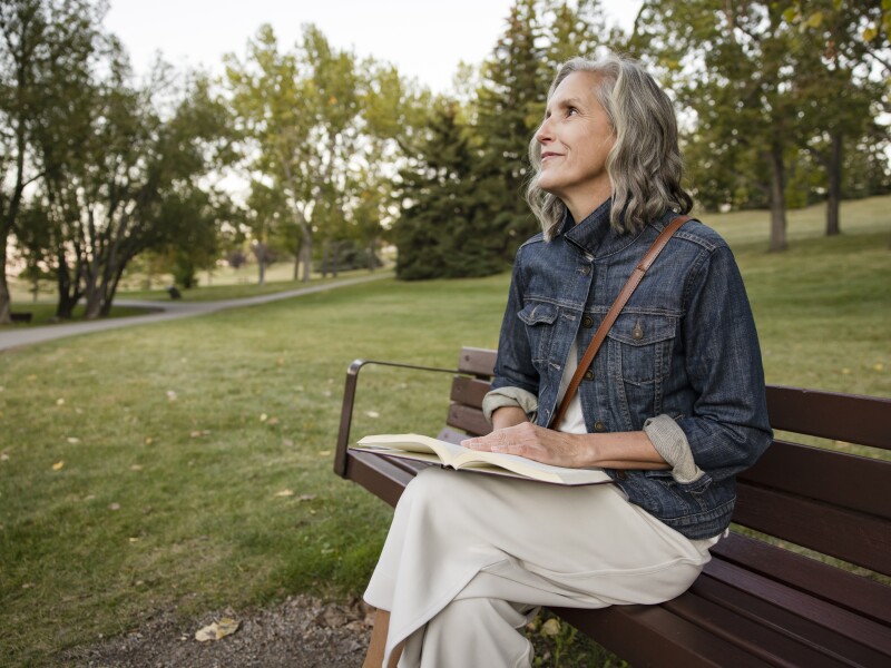Happy senior woman reading book on park bench