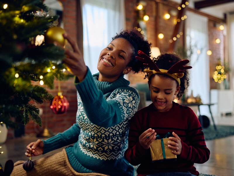 Happy black woman decorating Christmas tree with her daughter at home.