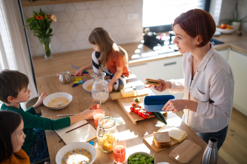 Mother of three little children preparing breakfast in kitchen at home.