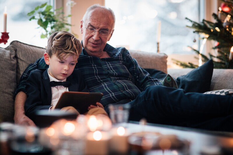 Grandfather looking at digital tablet while sitting with grandson in living room during Christmas