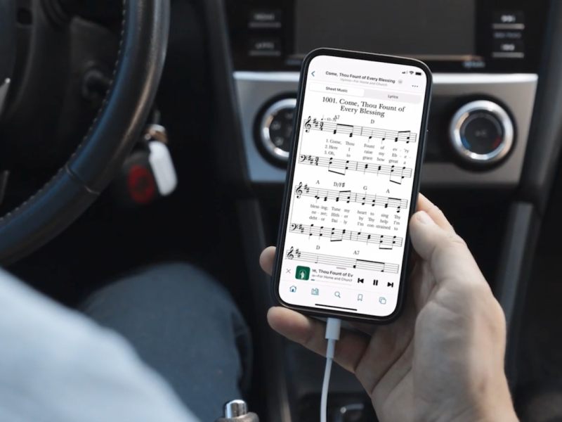 A smart phone shows digital sheet music for “Come, Thou Fount of Every Blessing.”