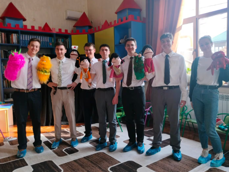 Six young men and one young woman hold puppets inside a center for women and children who have suffered from domestic violence.