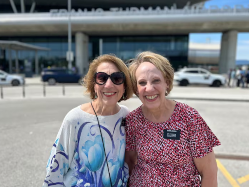 Two LDS senior sister missionaries smile in front of an airport in Croatia.