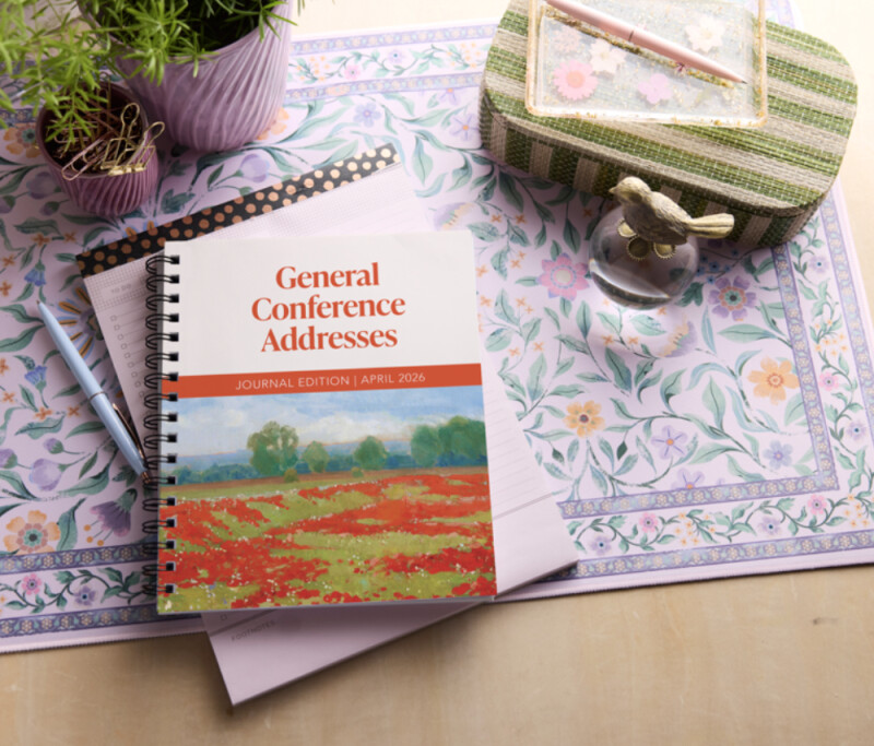 Un libro titulado "Discursos de la Conferencia General: Edición Journal, abril 2026" se encuentra sobre una mesa rodeado de objetos de temática floral.