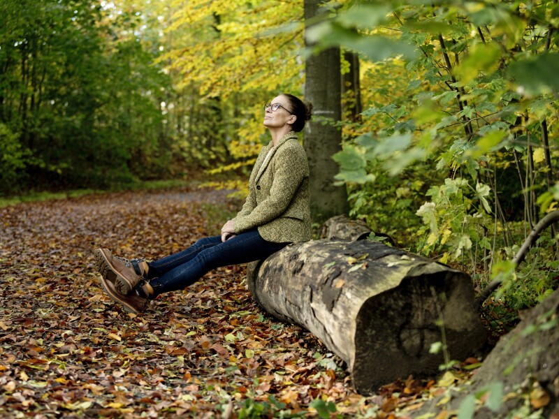 Mature woman sitting on a tree trunk in a autumn forest