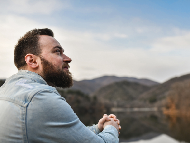 A bearded man clasping his hands and looking hopefully toward the sky