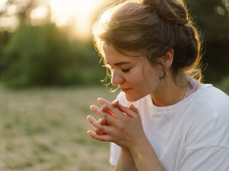A woman praying outside in a field