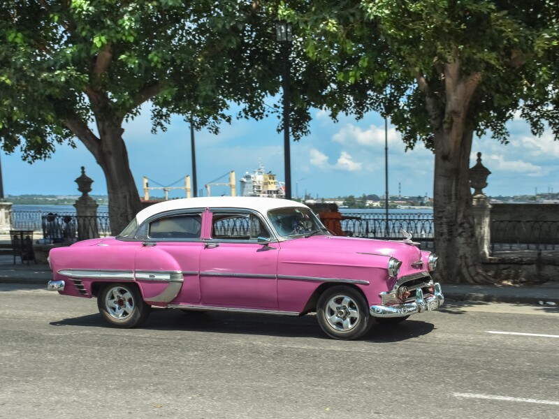 Real Cuban city life image with a pink vintage car riding by Havana's harbor