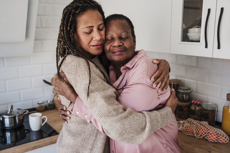 Woman with eyes closed embracing mother in kitchen at home