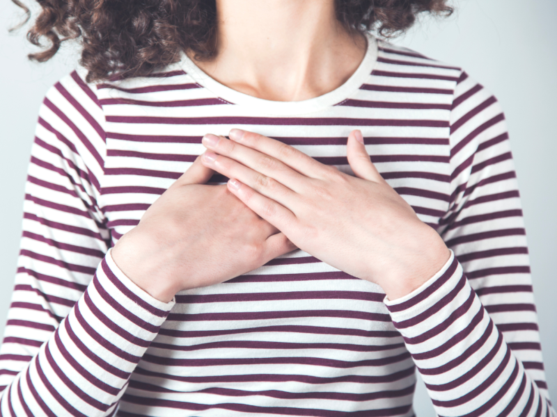 A woman wearing a striped shirt holds her hands over her heart.